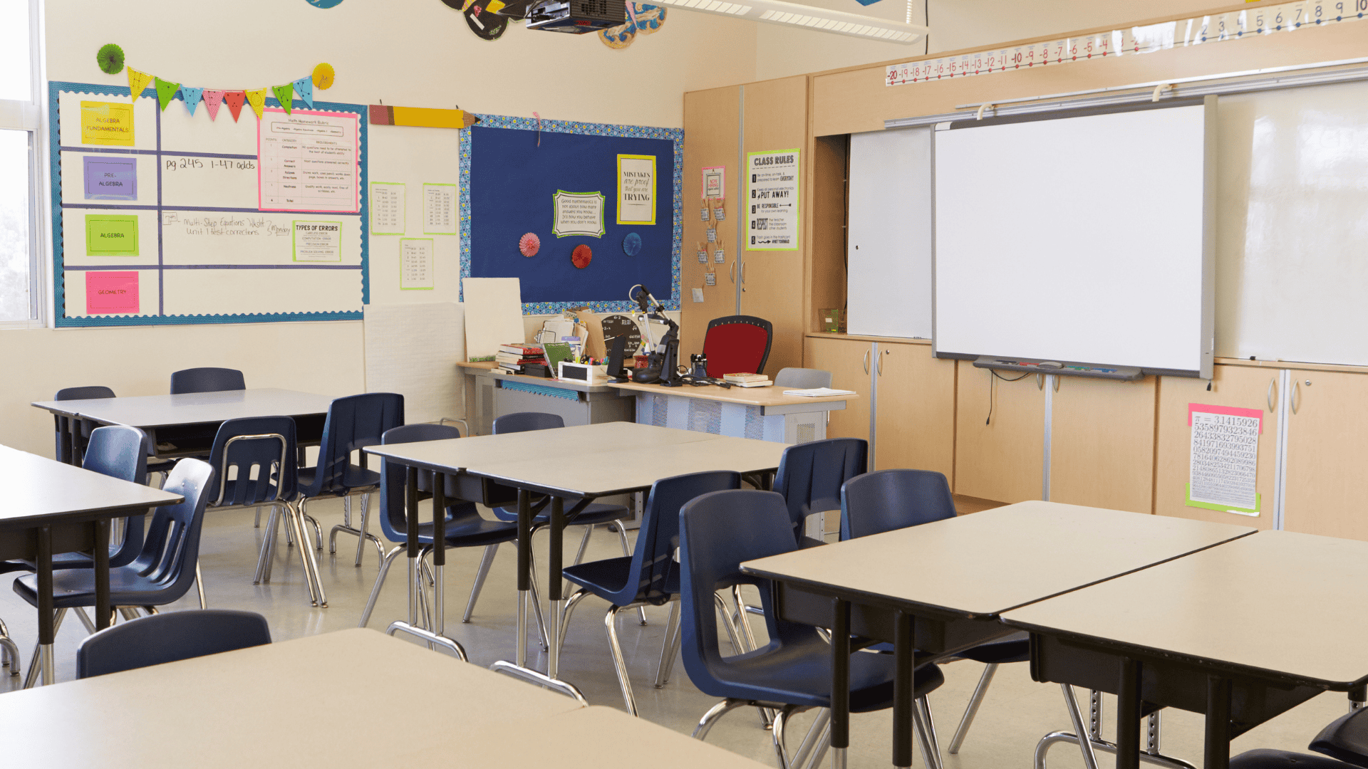 An image of an empty classroom. The teacher's desk sits at the far corner of the room, at the centre of the image.