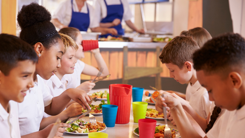 Primary school-aged children eating at a table in a school cafeteria.