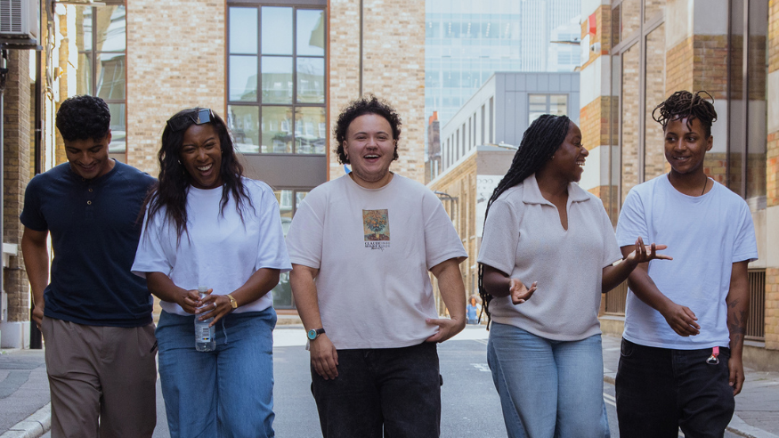 Five young people walking down a London street. They are all smiling and in conversation with one another. The image appears hopeful.