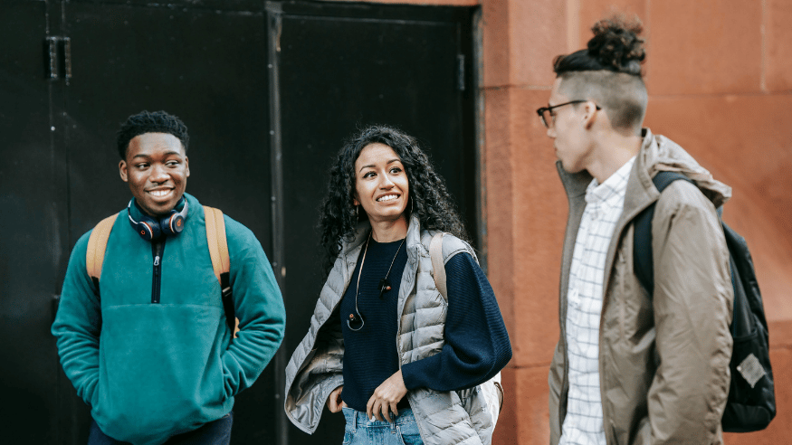 Three young adults engaging in friendly conversation outdoors, showcasing diverse styles and joy.