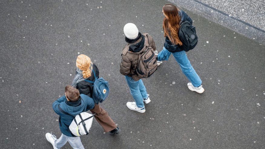 Young people walking together. Camera angle over the top of them, so you can't see their faces. They are walking on tarmac.